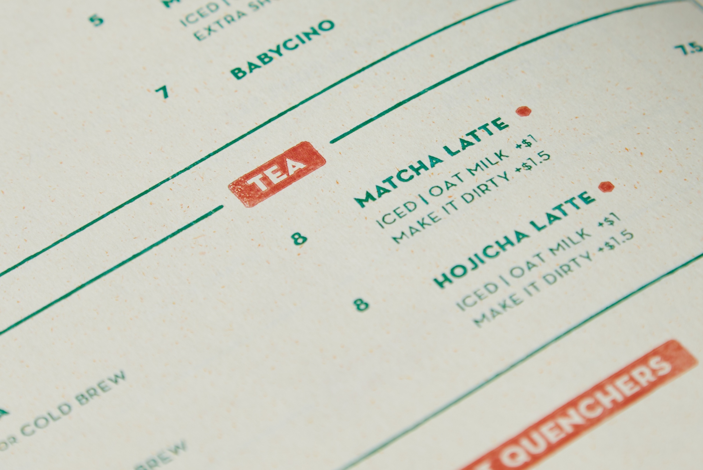 Extreme close-up of a Café Natsu menu page — curved green section rules, TEA and QUENCHERS coral rubber-stamp category headers, drink names in bold green Neutraface