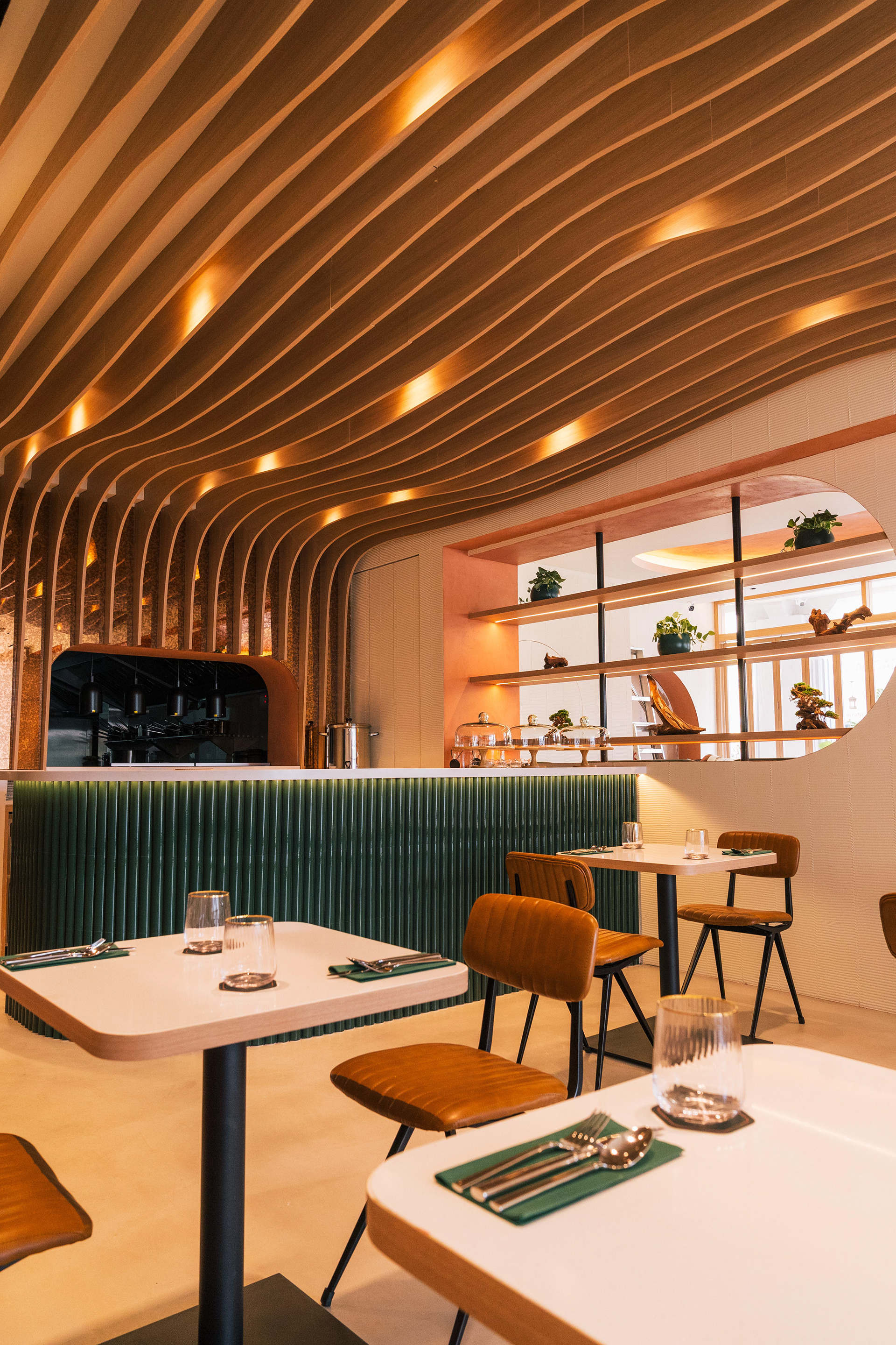 Bar counter area — sweeping undulating timber-slat ceiling with warm recessed lighting, green fluted tile bar fascia, white tables set with green napkins