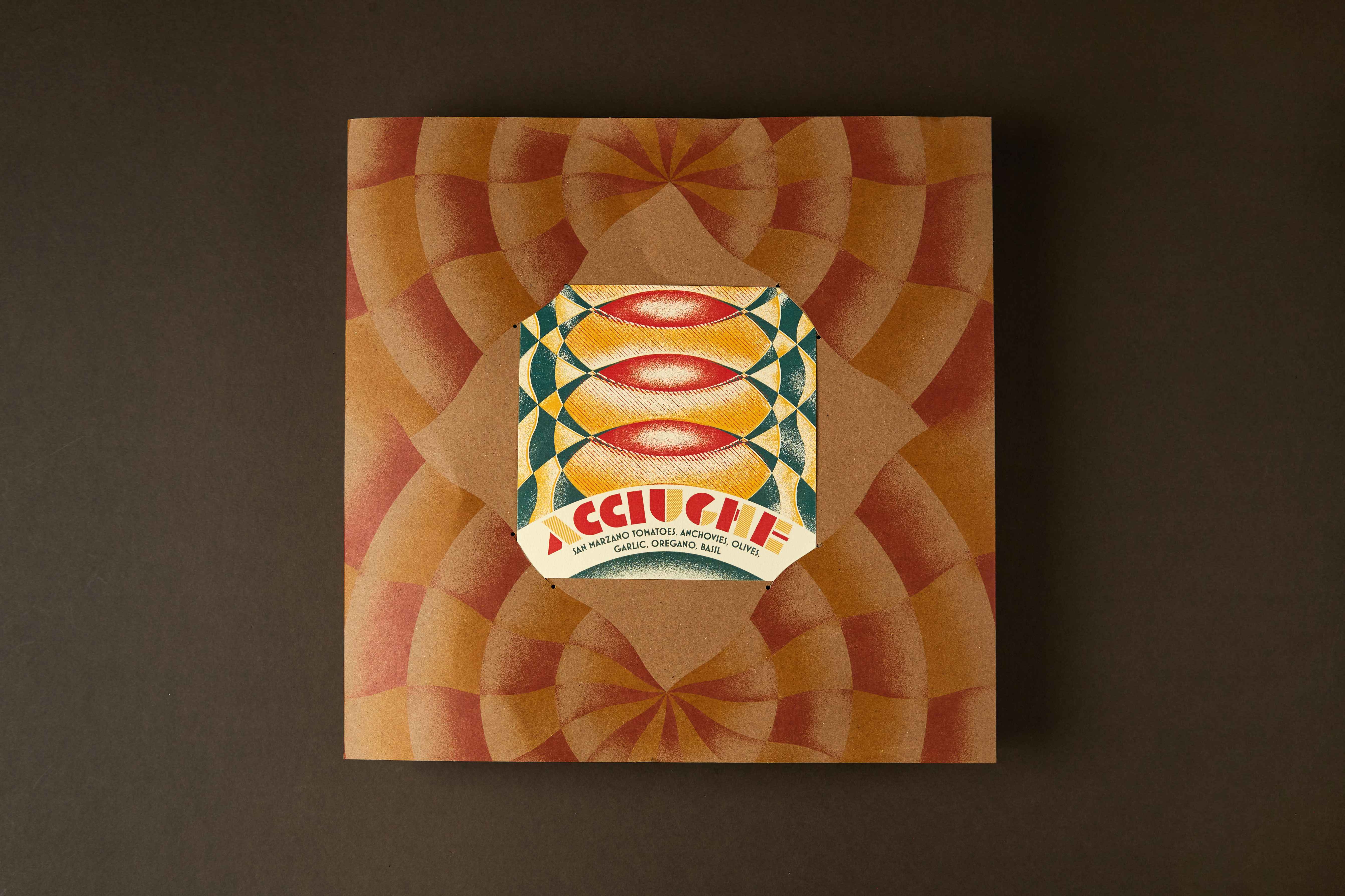 Top-down kraft box with a kaleidoscopic print and an ACCIUGHE pizza label on a dark surface