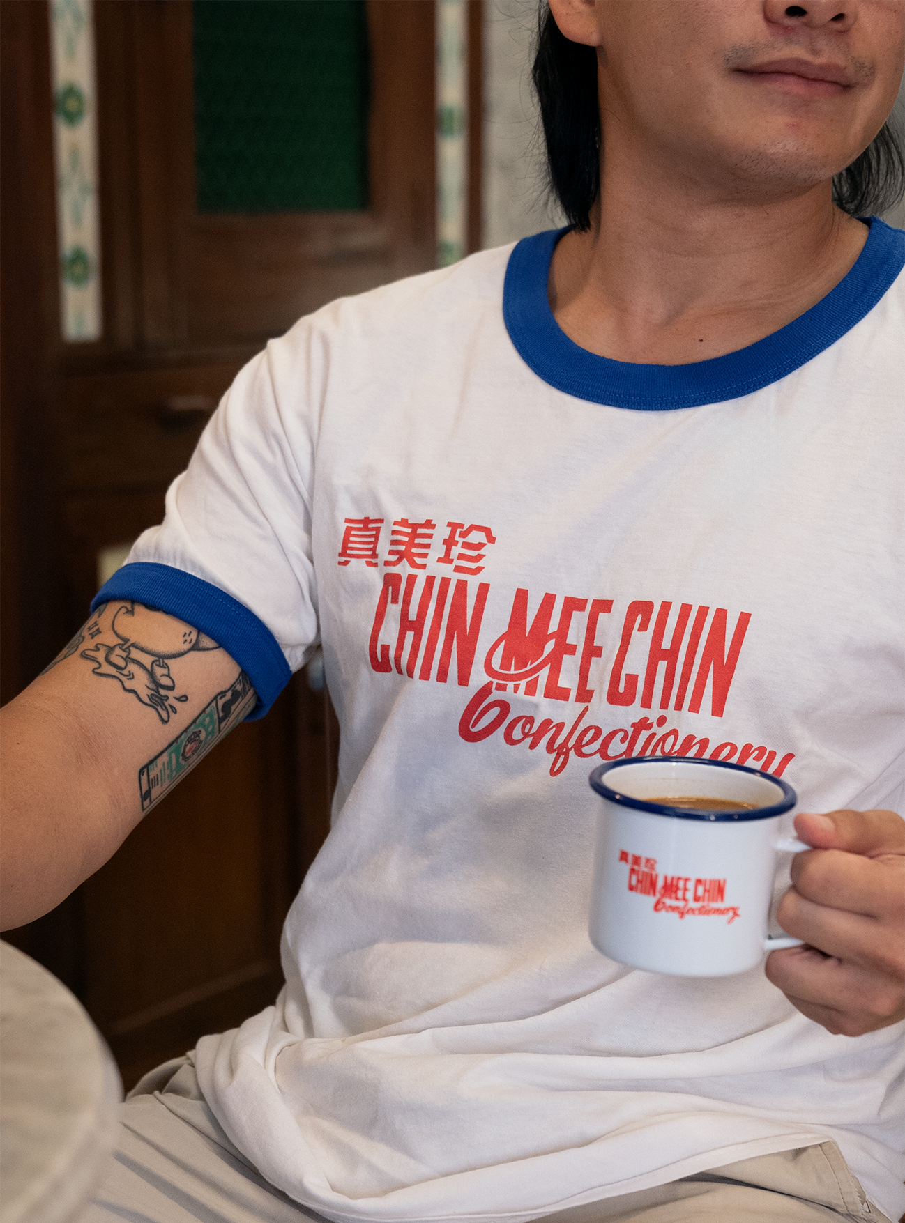 Man in CMC white-and-blue ringer tee holding a branded enamel kopi mug