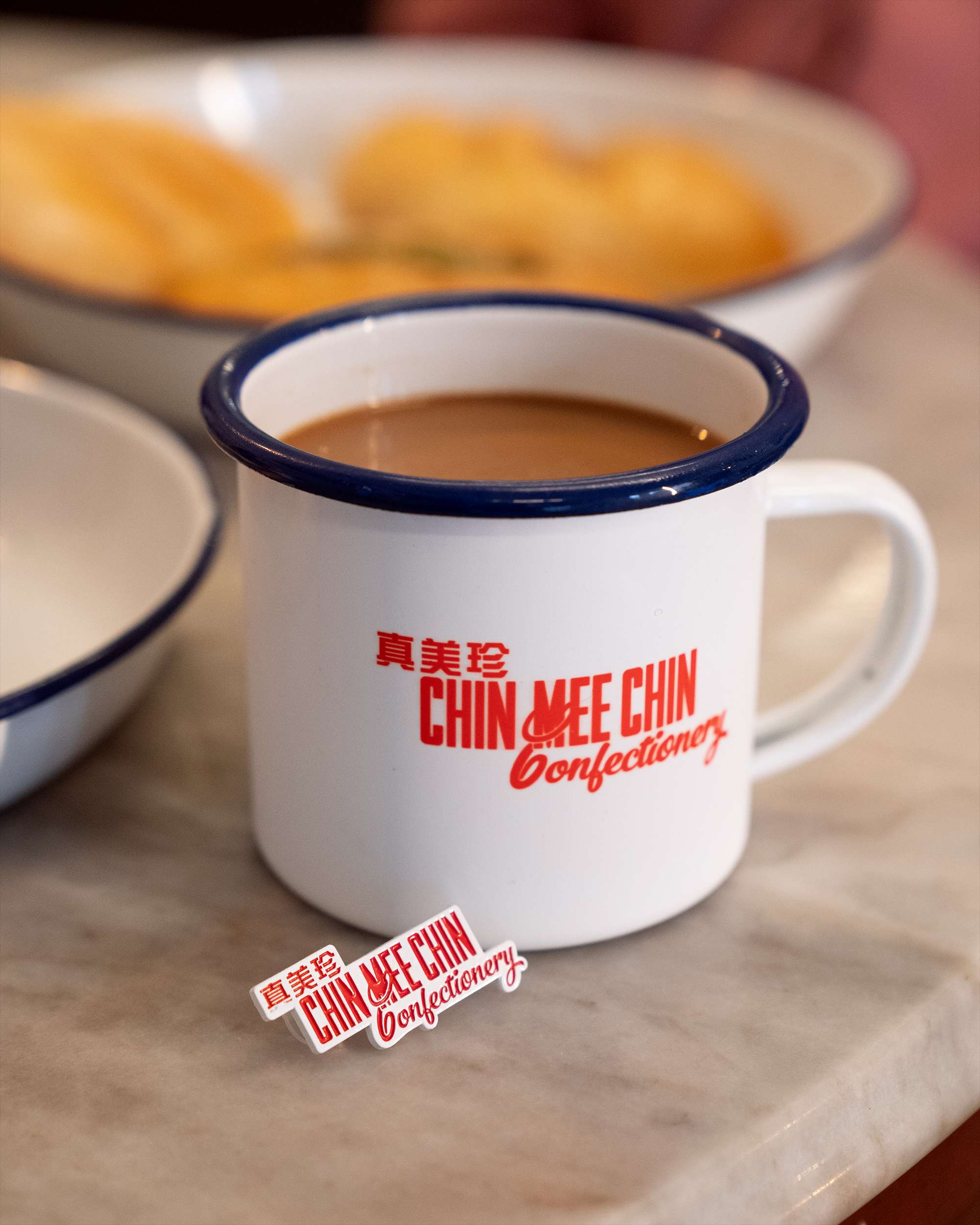 Close-up of the CMC enamel kopi mug and logo sticker on a marble café table