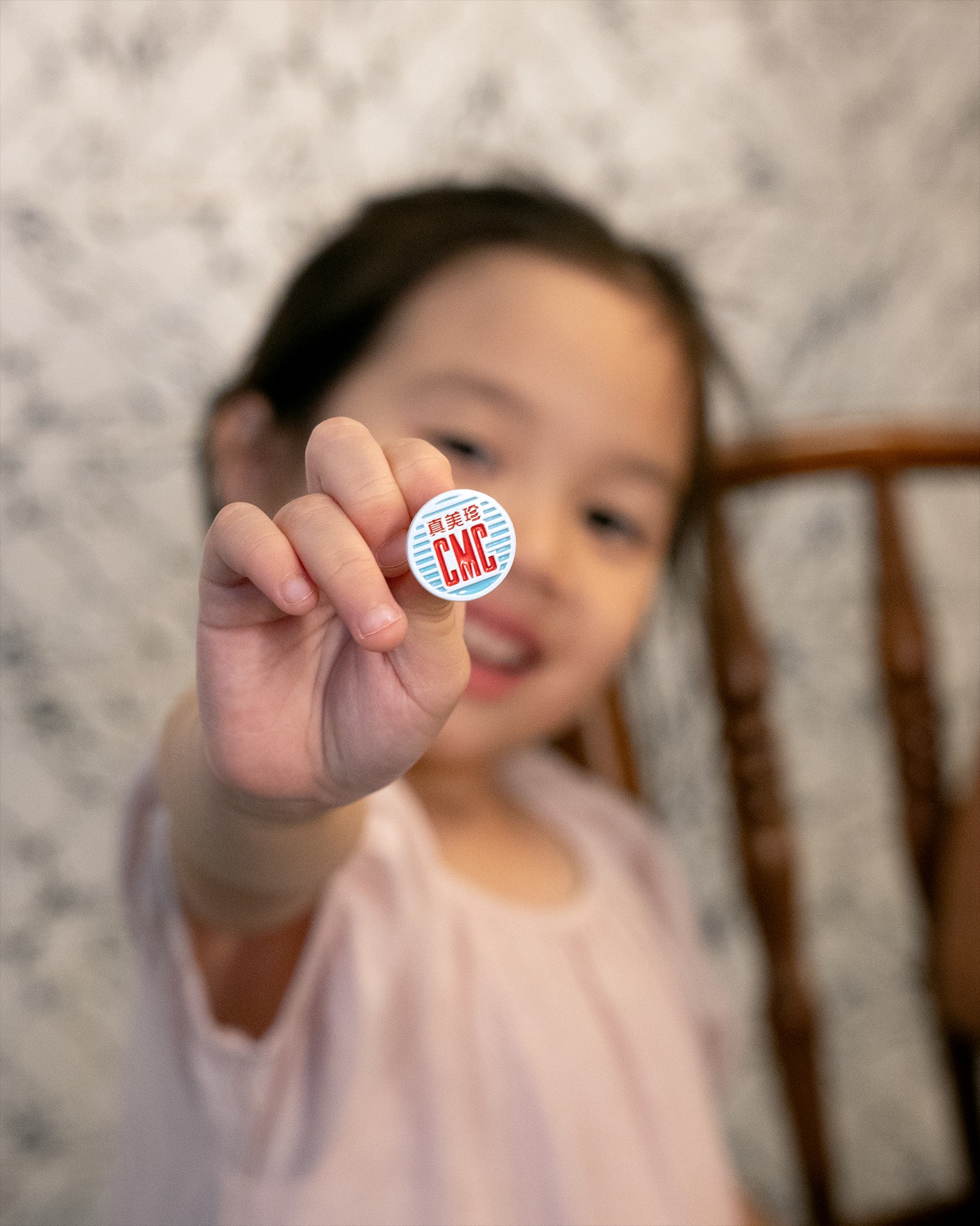Young girl holding a tiny CMC enamel pin badge up to the camera, bokeh background