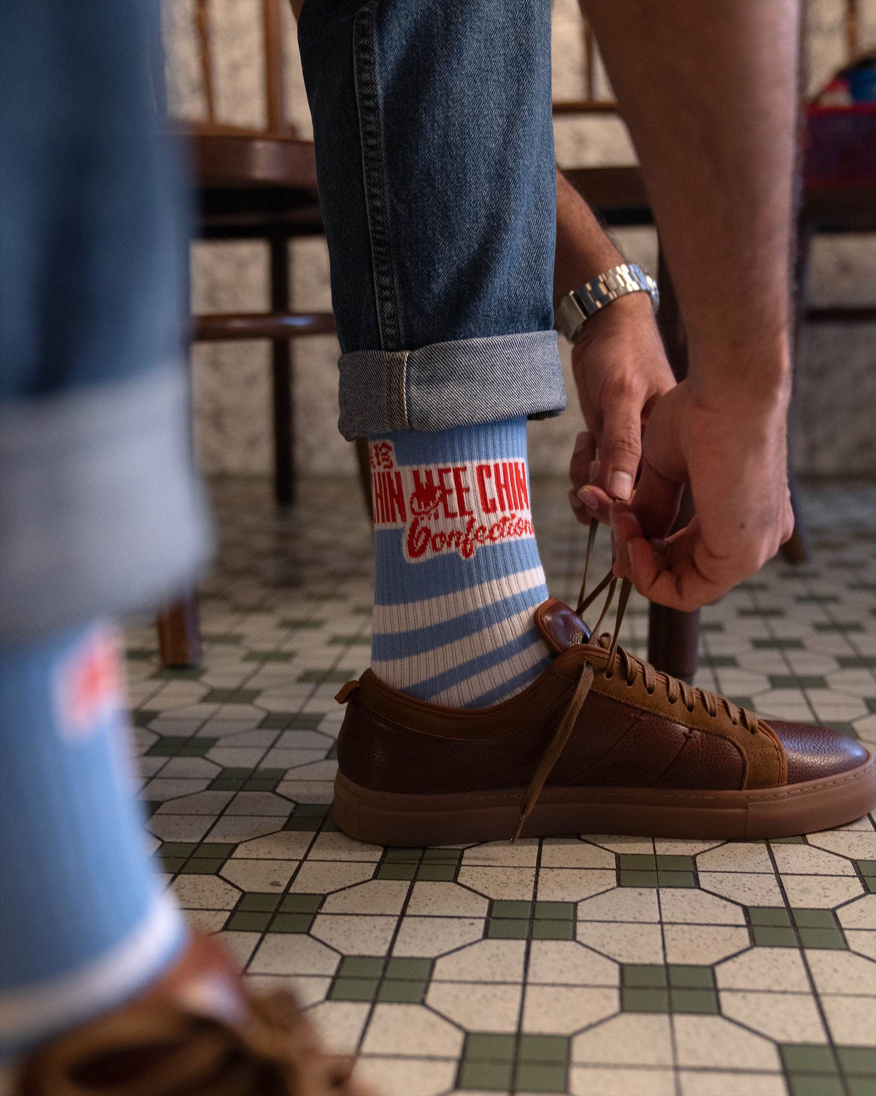 Person tying shoelace wearing CMC blue-striped socks, on the original hexagonal tile floor