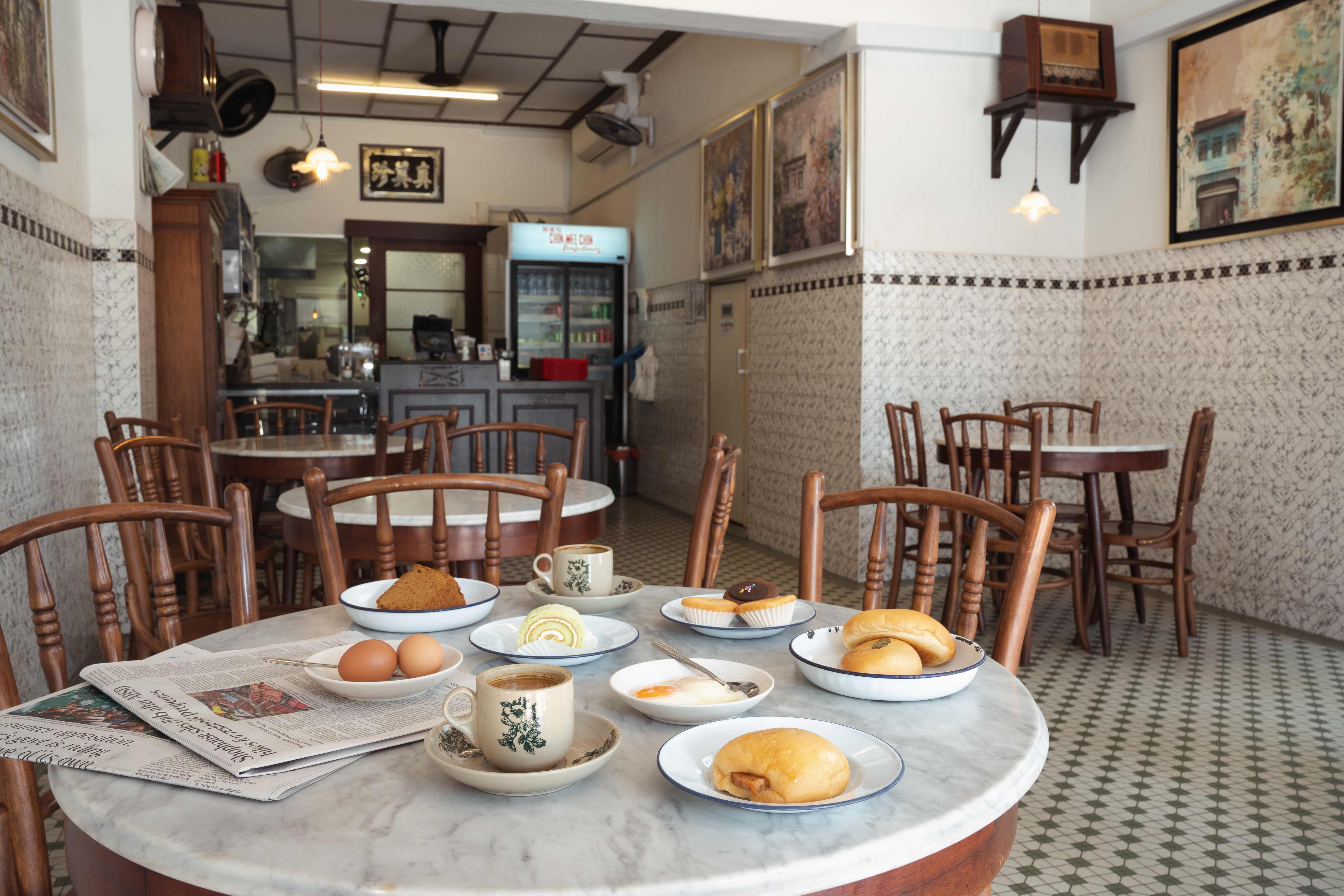 Original café interior — marble round tables, bentwood chairs, pastries and kopi, vintage paintings, and an old radio on a shelf