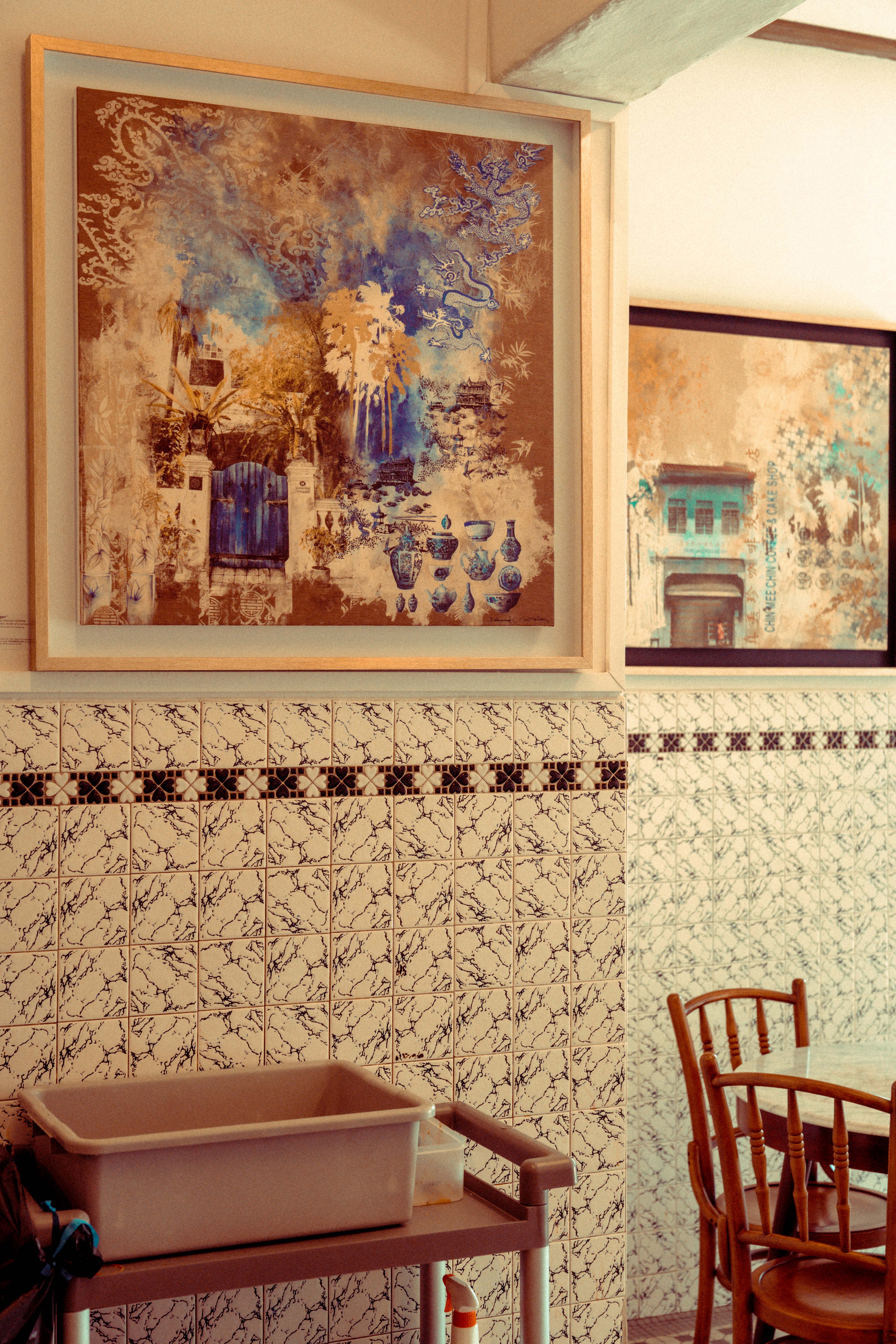 Two framed heritage artworks — a blue-and-gold dragon and garden scene beside the Chin Mee Chin shophouse print — hung above patterned marble tiles