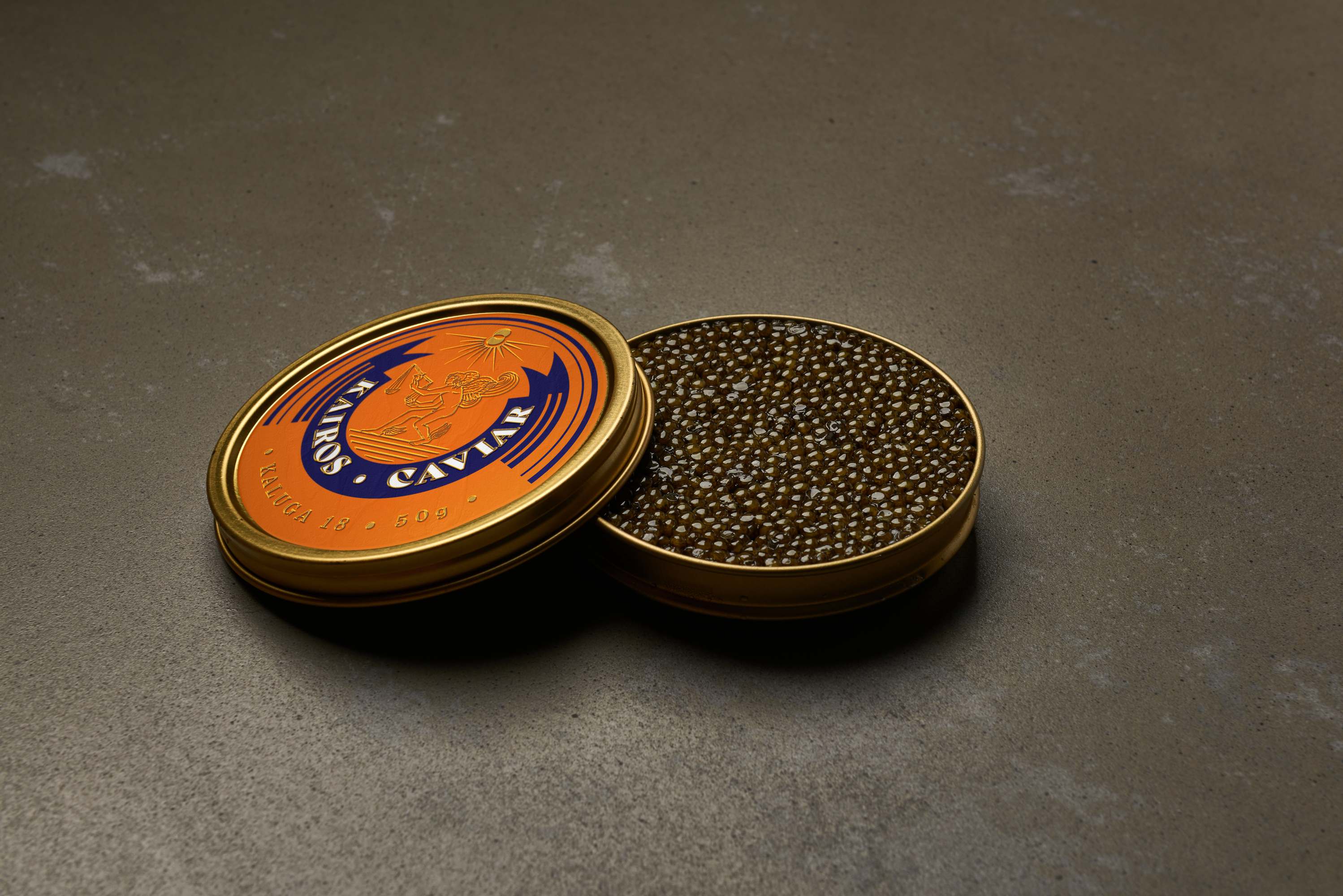 An open orange Kairos Caviar tin with its lid resting beside it, revealing glossy dark Kaluga caviar