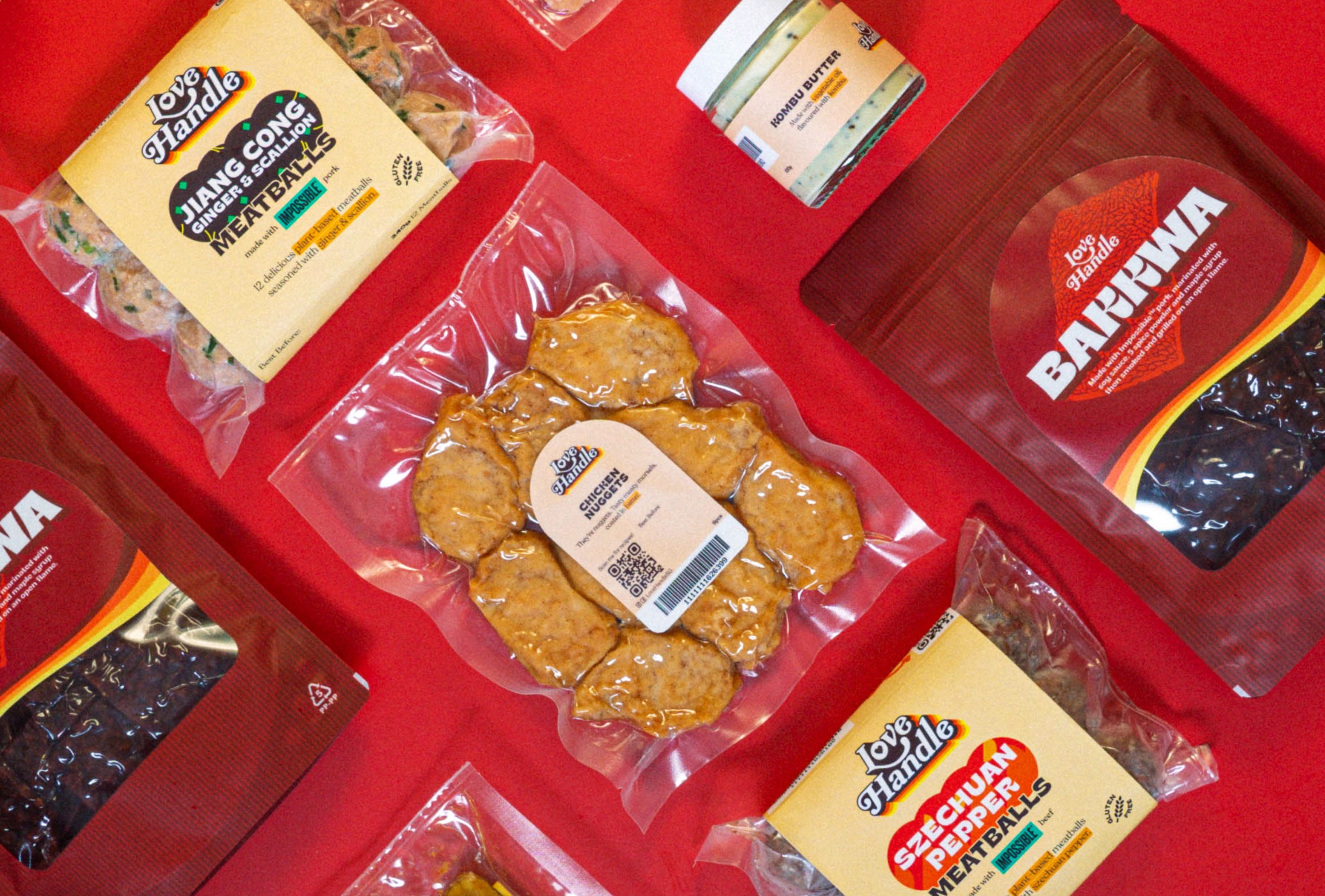 Flat-lay of Love Handle plant-based retail products on red — Jiang Cong Ginger & Scallion meatballs, Chicken Nuggets, Bakkwa, Szechuan Pepper meatballs and a Kombu Butter jar