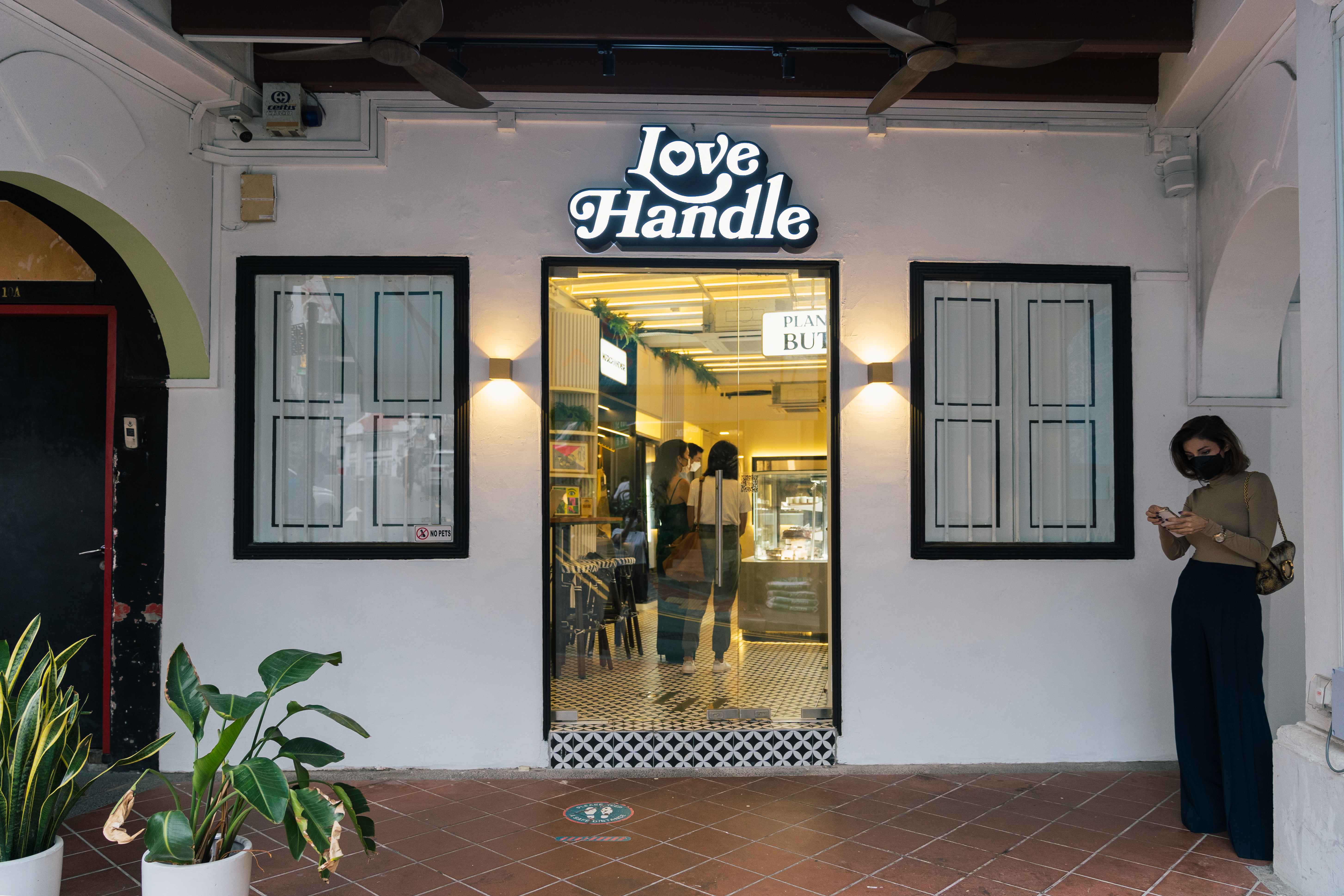 Love Handle storefront on Ann Siang Hill — white shophouse facade with an illuminated black-and-white retro Love Handle logo sign above a glass door, potted plants on the terracotta forecourt