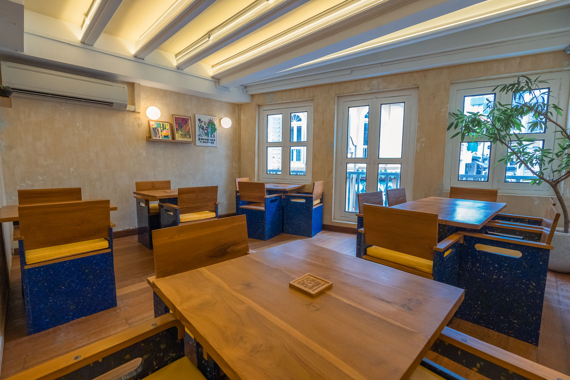 Upstairs dining room — blue recycled-plastic cube seating with yellow cushions, timber tables, framed retro posters and shuttered windows