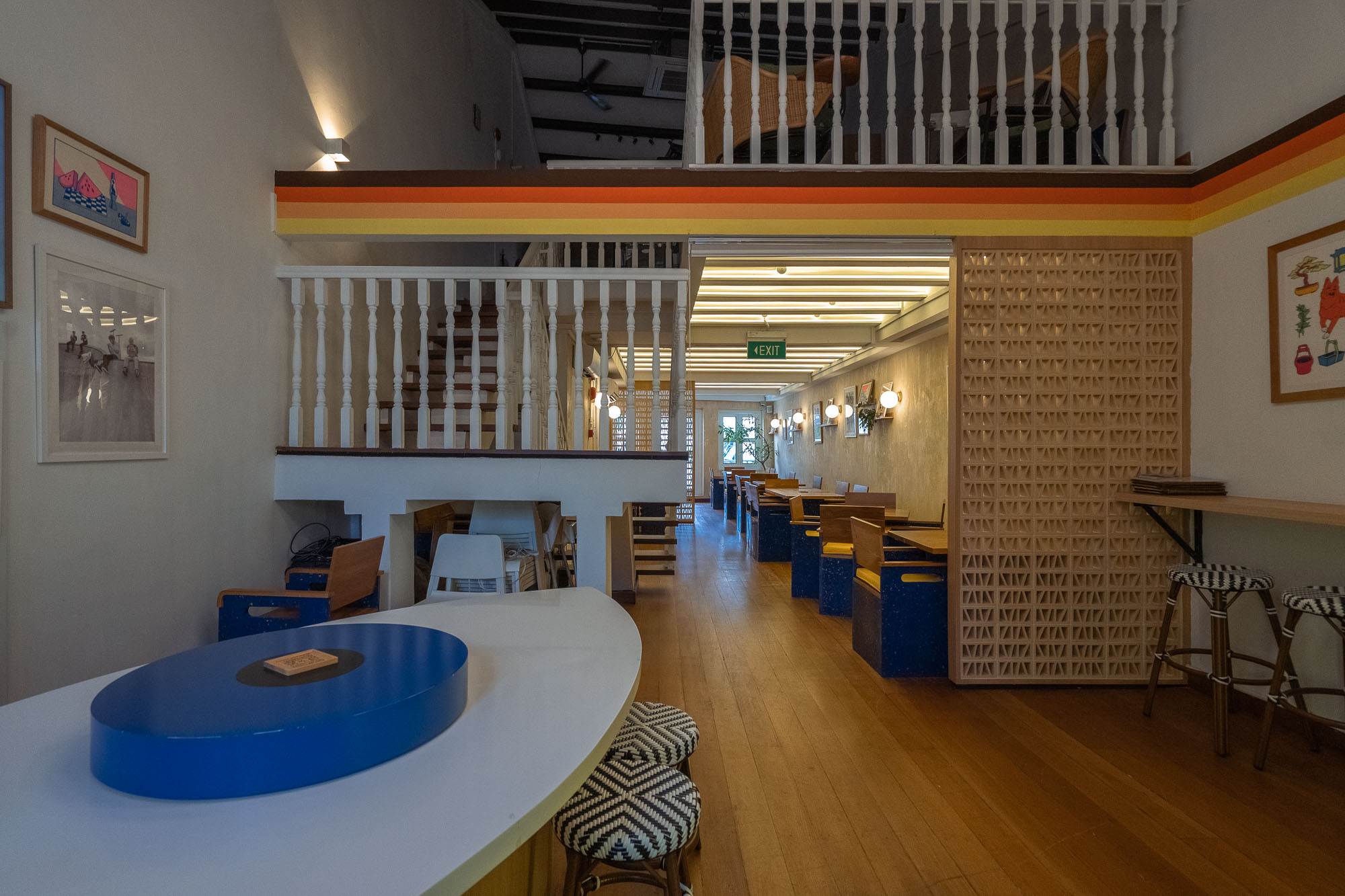 Mezzanine level — retro rainbow stripe wall trim, white spindle balustrade and stairs, blue bench seating and a breeze-block screen