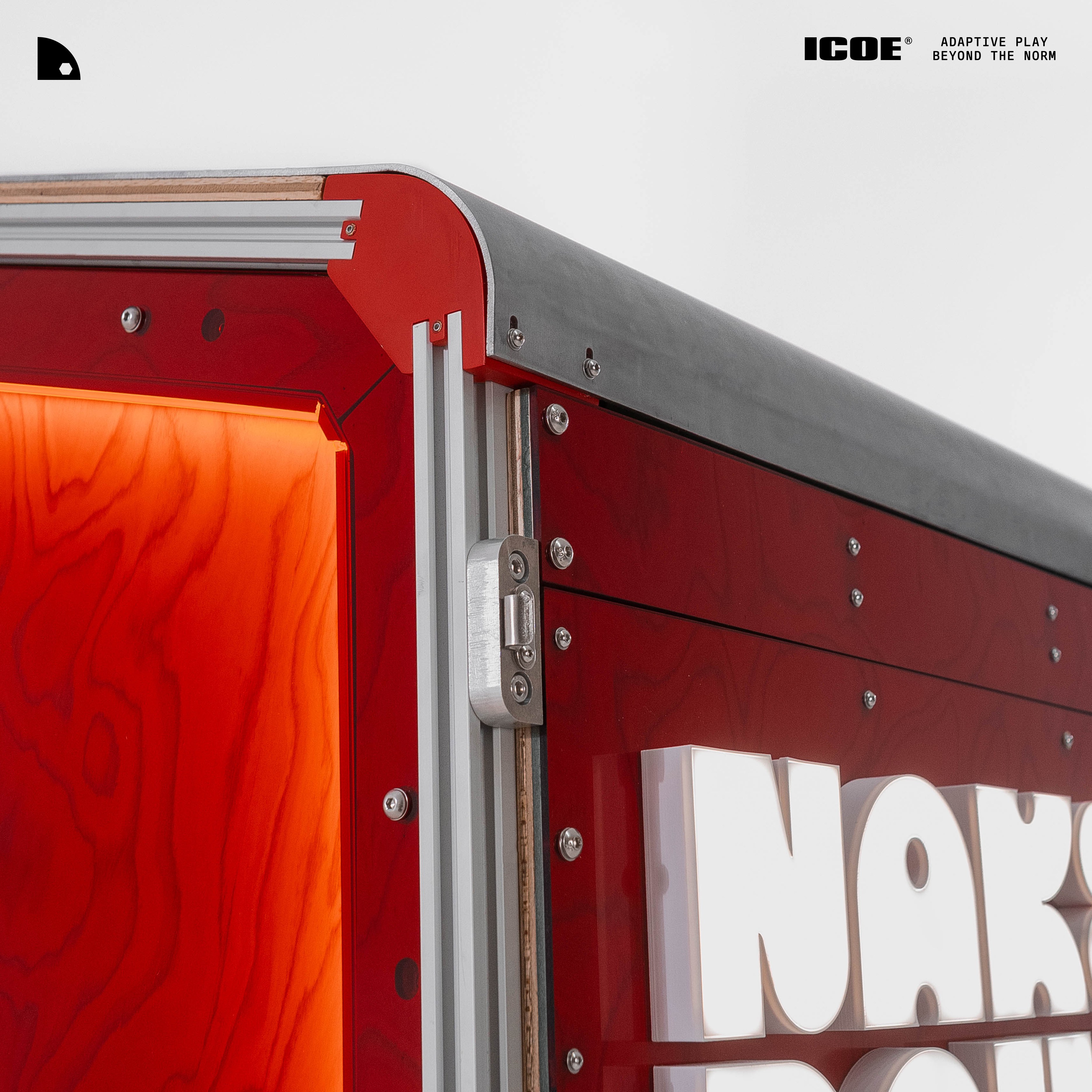 Extreme close-up of the booth's top corner — aluminium extrusion frame, stainless hinge, red woodgrain panels, a glowing orange acrylic edge and partial NAK… signage