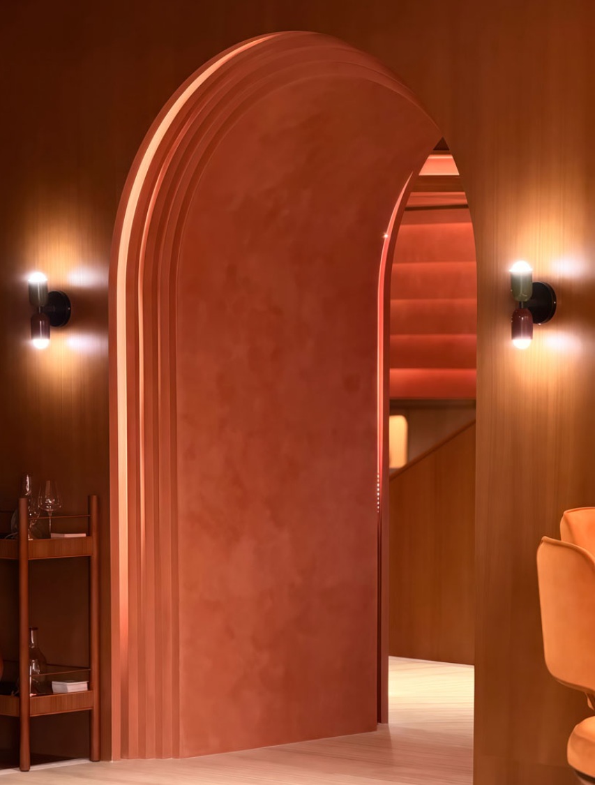 Terracotta plaster archway with wall sconces, a timber bar cart, and stairs beyond