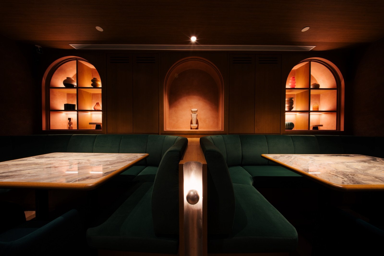 Intimate private dining booths with green velvet banquettes, marble tables, and arched lit niches displaying ceramics