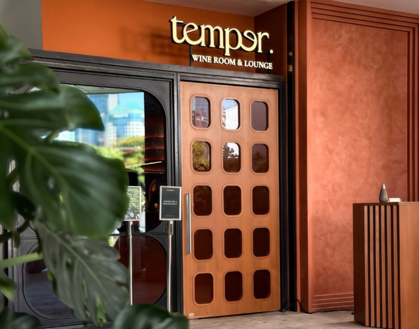 Temper Wine Room & Lounge entrance — illuminated signage above a wood-slatted glass door set in a terracotta facade